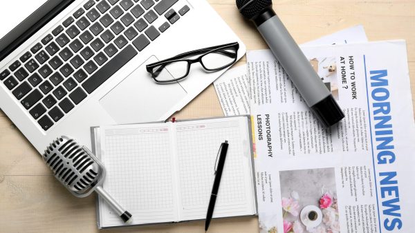 Laptop,With,Eyeglasses,,Microphones,,Notebook,And,Newspapers,On,Light,Wooden